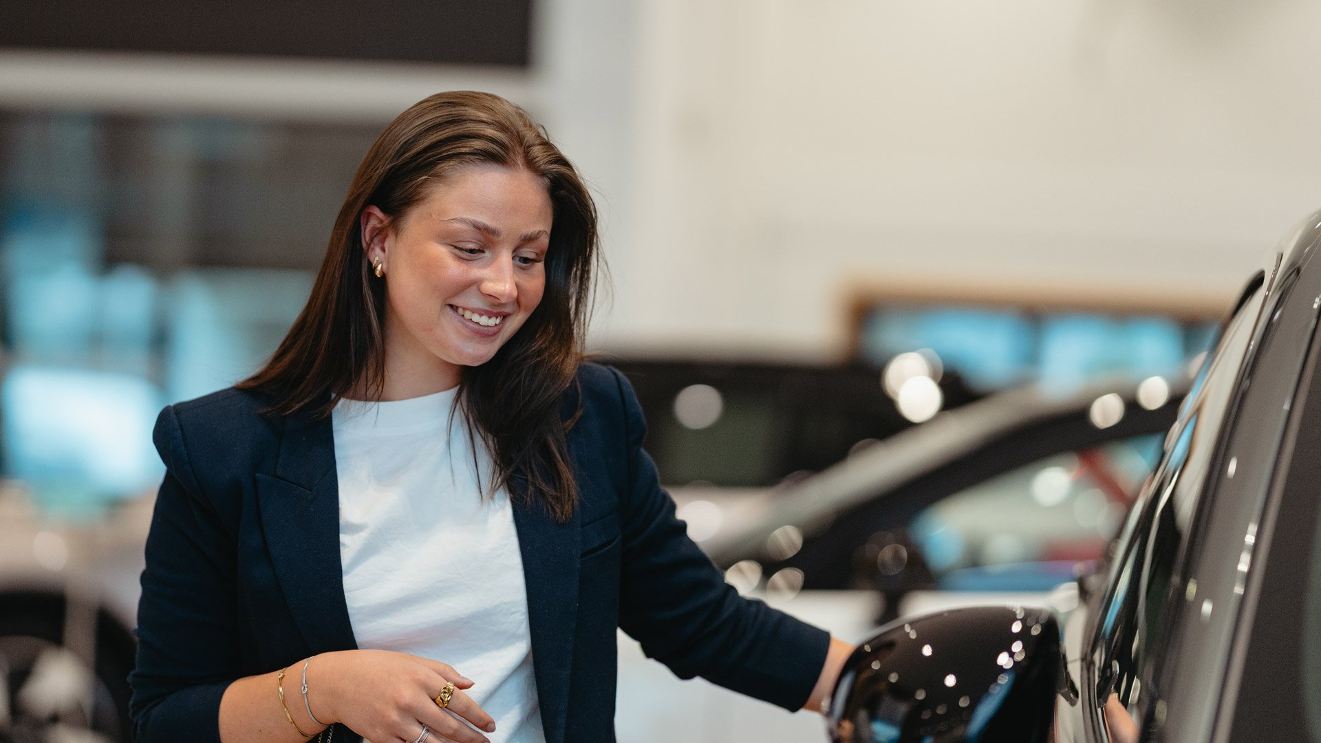 En smilene Nathalie Skoglund hos Frydenbø Bil Kokstad står utenfor en bil inne i butikken