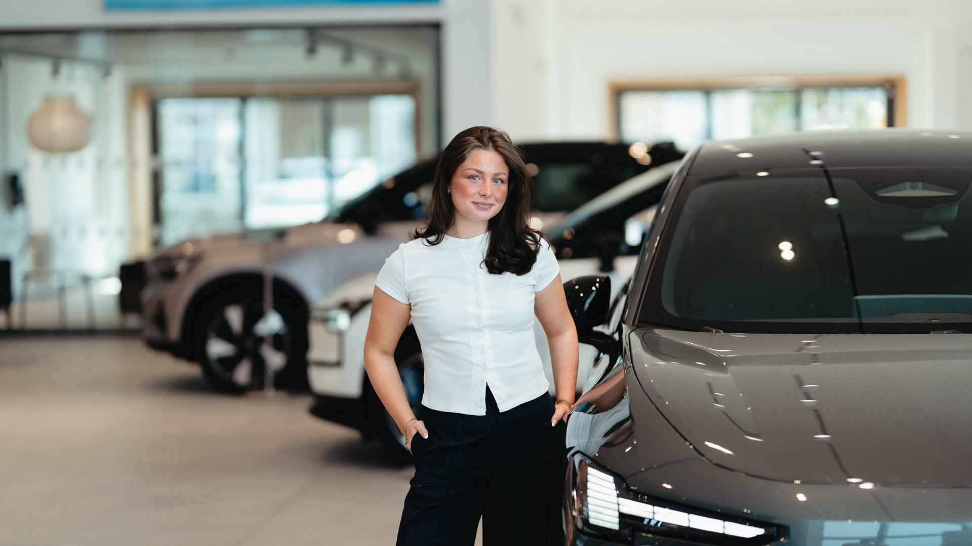 Nathalie Skoglund hos Frydenbø Bil på Kokstad står i salgslokalet sammen med en Volvo EX60