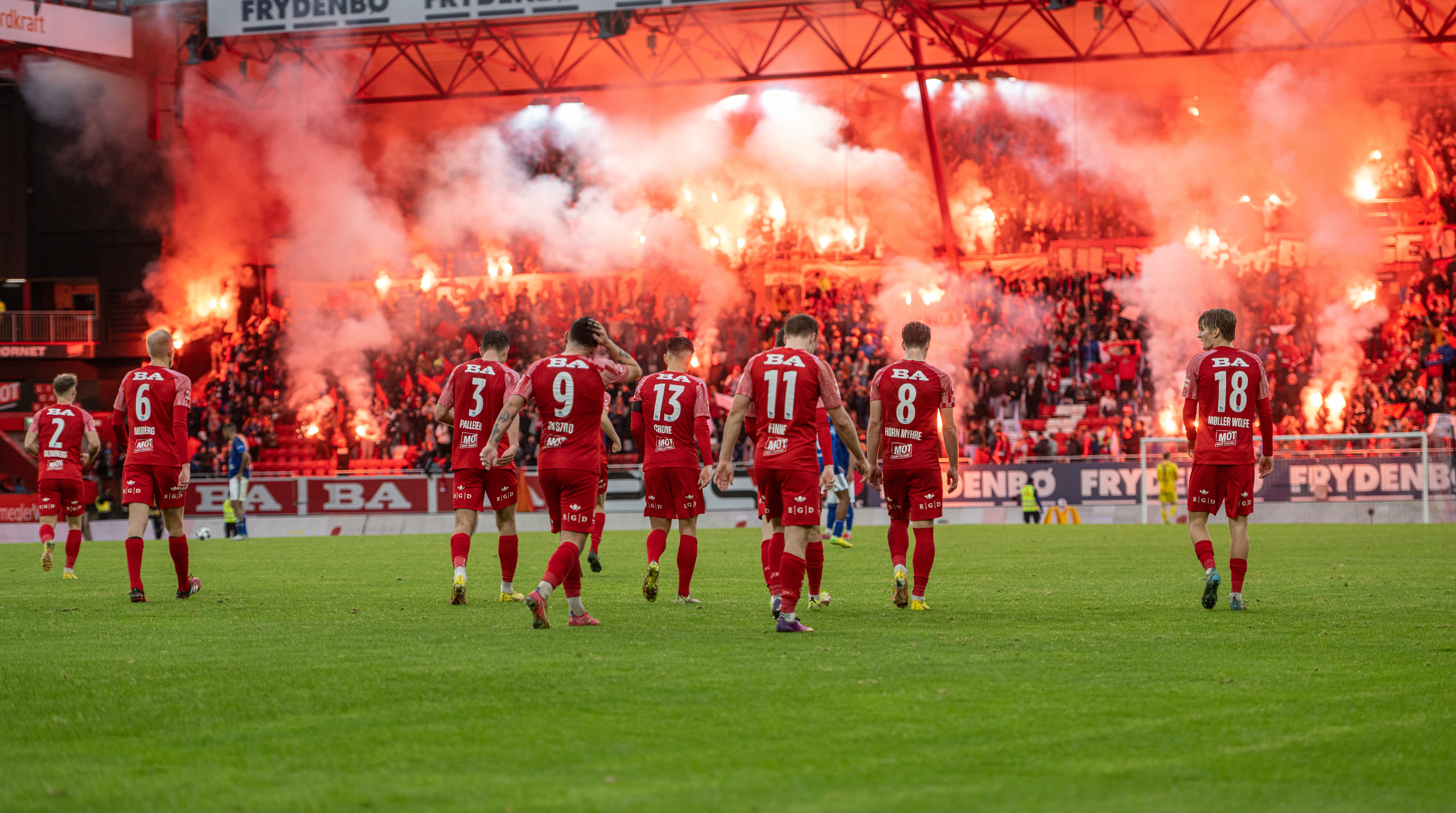 Brannspillere med en opplyst Frydenbø-tribune i bakgrunnen. 